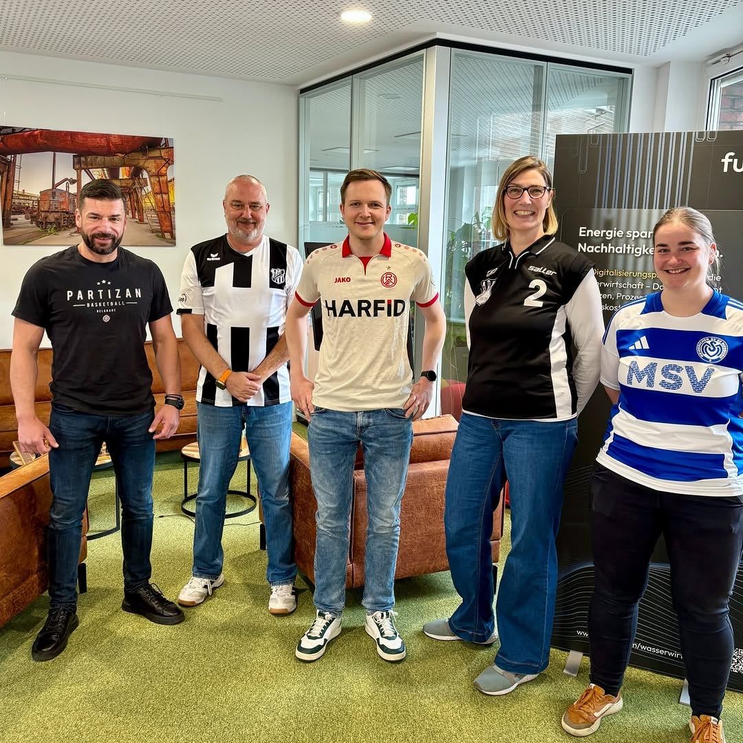 Fünf Kolleginnen und Kollegen in Fußballtrikots verschiedener Vereine im Büro